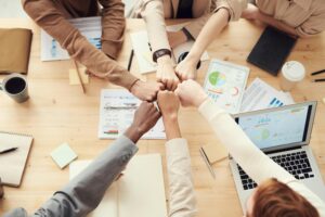 Top view of a diverse team fist bumping over a meeting table with paperwork and laptops, symbolizing teamwork.