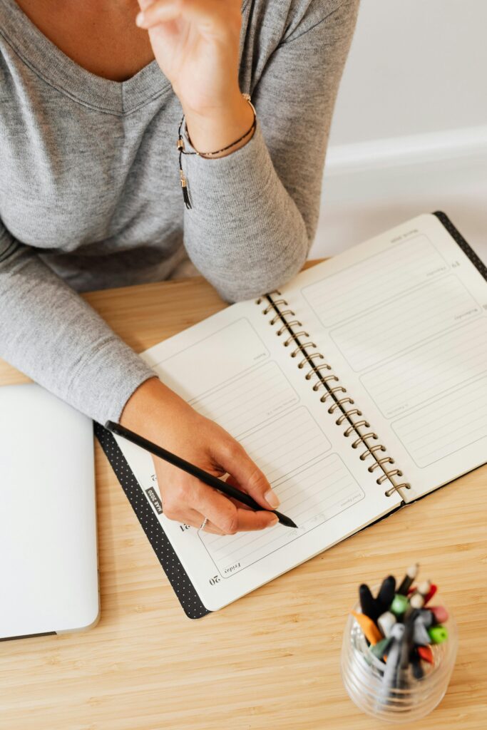 Overhead view of a woman writing in a planner, ideal for productivity concepts.